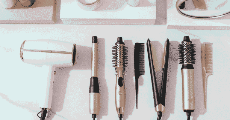 Flat lay of the best hair styling tools for 2025, including hair dryer, curling wand, and hot brush in a modern, minimal blush pink and white setting, designed for achieving professional salon results at home.