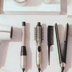 Flat lay of the best hair tools for styling in 2025, including hair dryer, curling wand, and hot brush in a modern, minimal blush pink and white setting, designed for achieving professional salon results at home.