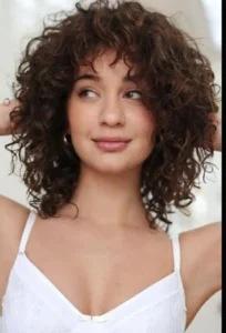 Woman with layered curly shag haircut, full of volume and bounce, trending in 2025.