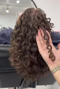 Woman with long, defined curly hairstyle, shiny and frizz free curls trending in 2025.