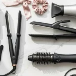 Flat lay of best hair styling tools for women in 2025, including curling iron, blow dryer, straightener, and hair brush
