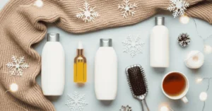 Flat lay of winter hair care essentials including conditioner, hair oil, and brush, styled with seasonal elements like cozy scarf, eucalyptus, snowflakes, and soft lighting for a winter beauty blog post.